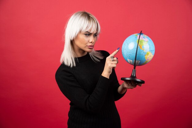 Junge Frau, die einen Globus auf einem roten Hintergrund zeigt. Hochwertiges Foto