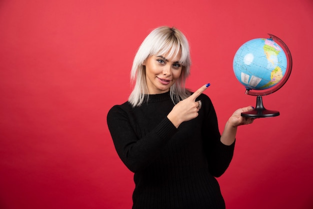Junge Frau, die einen Globus auf einem roten Hintergrund zeigt. Hochwertiges Foto