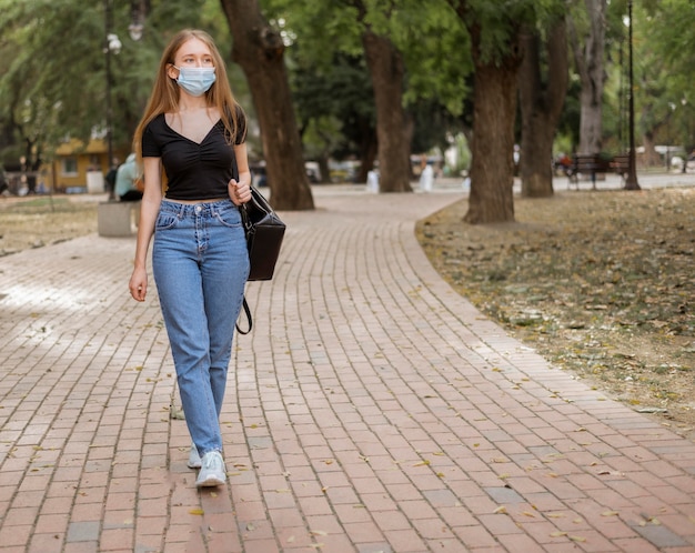 Kostenloses Foto junge frau, die einen spaziergang beim tragen der medizinischen maske hat