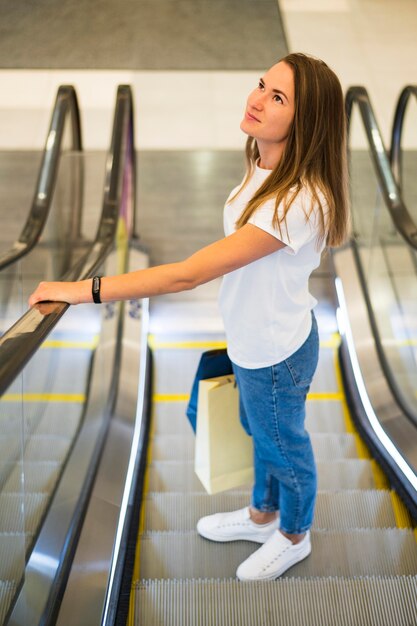 Junge Frau, die Einkaufstaschen auf der Rolltreppe hält