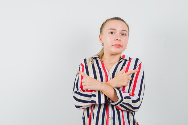 Junge Frau, die entgegengesetzte Richtungen in gestreifter Bluse zeigt und hübsch aussieht