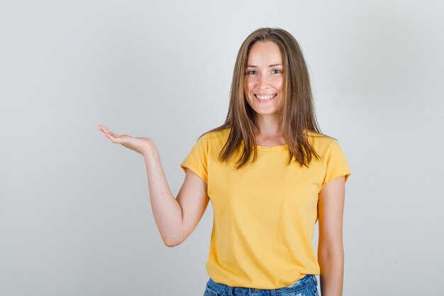 Junge Frau, die erhabene Handfläche im T-Shirt, in den Shorts hält und fröhlich aussieht