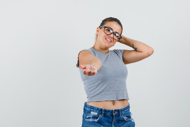 Junge Frau, die etwas in der Hand in T-Shirt, Shorts und schön aussehend streckt