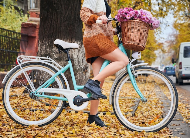 Junge Frau, die Fahrrad mit Blumen auf der Herbststraße fährt