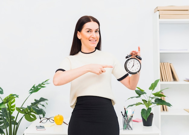 Kostenloses Foto junge frau, die finger auf uhr im büro zeigt