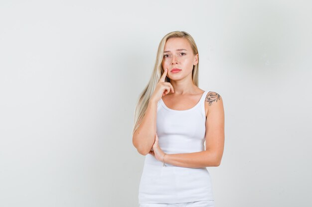 Junge Frau, die Finger auf Wange im weißen Unterhemd, im Minirock hält und traurig schaut.