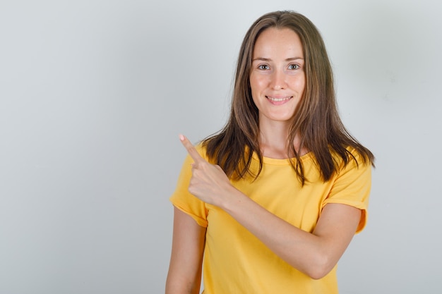 Junge Frau, die Finger im gelben T-Shirt nach hinten zeigt und fröhlich schaut