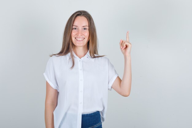 Junge Frau, die Finger zeigt und im weißen T-Shirt lächelt