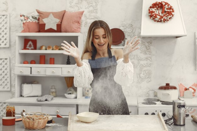 Junge Frau, die geformte Kekse für Weihnachten macht. Wohnzimmer mit Weihnachtsdekorationen im Hintergrund verziert. Frau in einer Schürze.