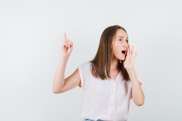 Junge Frau, die Geheimnis erzählt und Finger oben im T-Shirt, Vorderansicht zeigt.