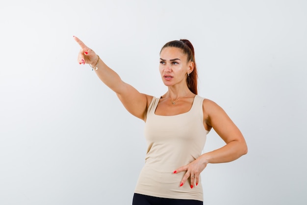 Junge Frau, die gerade in beige Trägershirt zeigt und zuversichtlich schaut. Vorderansicht.