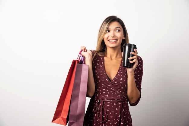 Junge Frau, die Geschäftstaschen und eine Tasse Getränk auf weißer Wand hält.