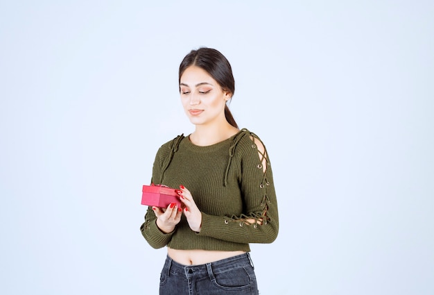 Junge Frau, die Geschenkbox auf weißem Hintergrund hält.