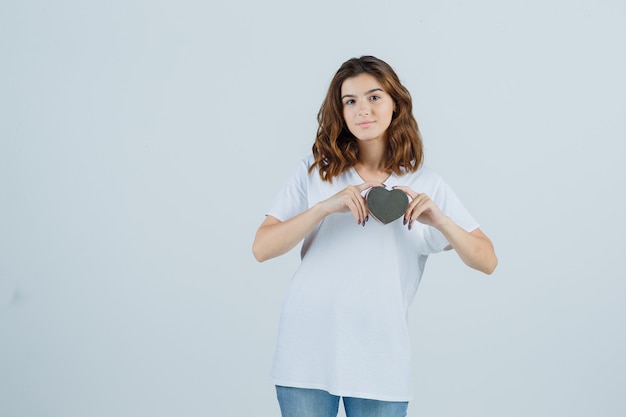 Junge Frau, die Geschenkbox in weißem T-Shirt, Jeans hält und selbstbewusst, Vorderansicht schaut.