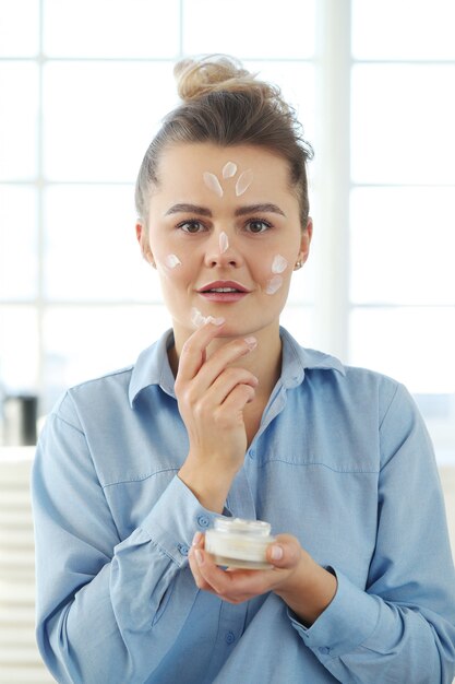 Junge Frau, die Gesichtscreme verbreitet. Hautpflegekonzept.