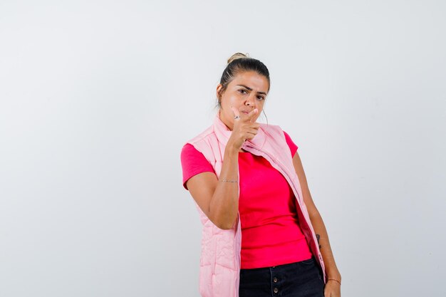 Junge Frau, die Gewehrgeste in rosa T-Shirt und Jacke zeigt und wütend aussieht