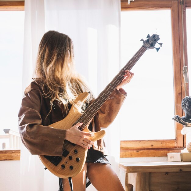 Junge Frau, die Gitarre nahe Fenster spielt