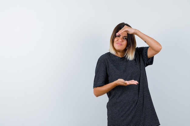 Junge Frau, die Größenzeichen im Polokleid zeigt und zuversichtlich schaut. Vorderansicht.