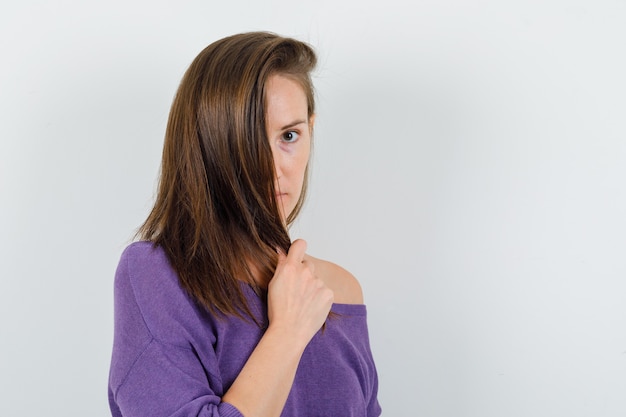 Junge Frau, die Haarsträhne im violetten Hemd, Vorderansicht hält.
