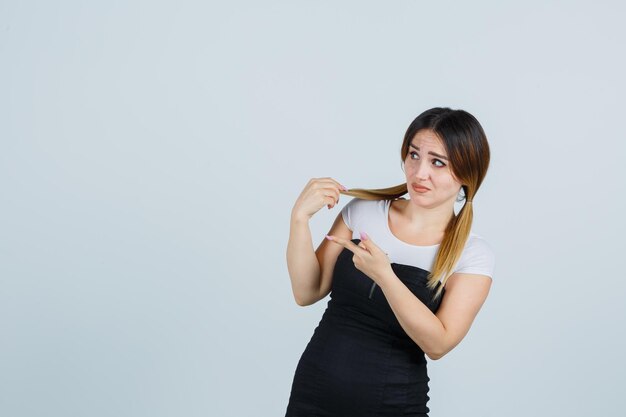 Junge Frau, die Haarsträhnen hält und auf die linke Seite zeigt