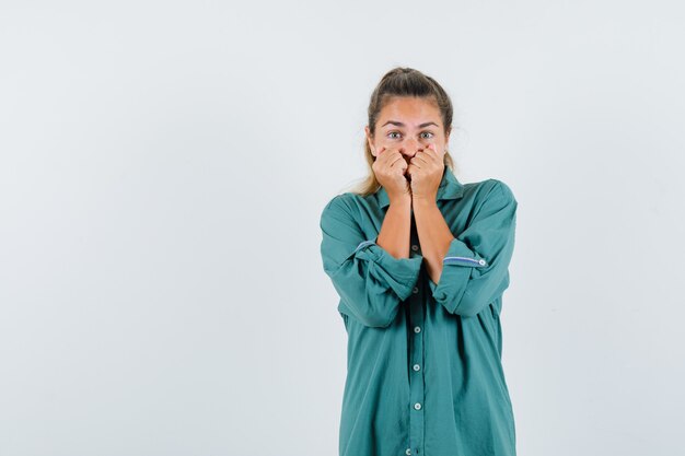 Junge Frau, die Hände auf ihrem Mund im blauen Hemd hält und ängstlich schaut