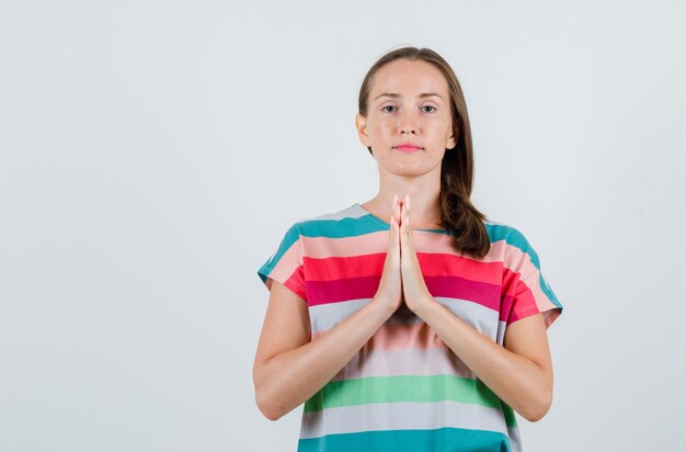 Junge Frau, die Hände in der Gebetsgeste im T-Shirt hält und friedlich schaut. Vorderansicht.