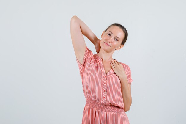 Junge Frau, die Hand am Hals im gestreiften Kleid hält und entspannt, Vorderansicht schaut.