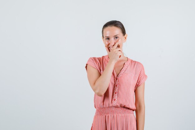 Junge Frau, die Hand auf Gesicht im gestreiften Kleid hält und glückliche Vorderansicht schaut.