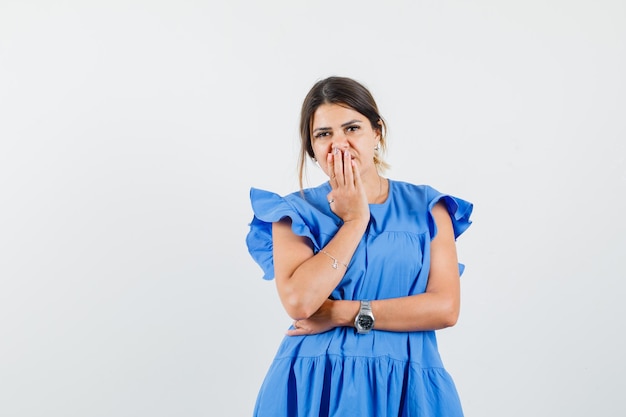 Junge frau, die hand auf mund im blauen kleid hält und enttäuscht schaut