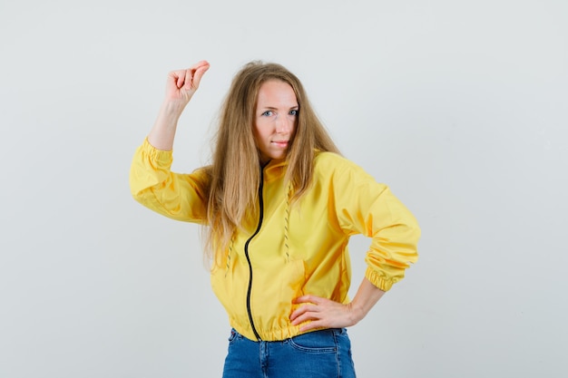 Kostenloses Foto junge frau, die hand auf taille hält und an der kamera in gelber bomberjacke und blauer jeans aufwirft und attraktive vorderansicht schaut.