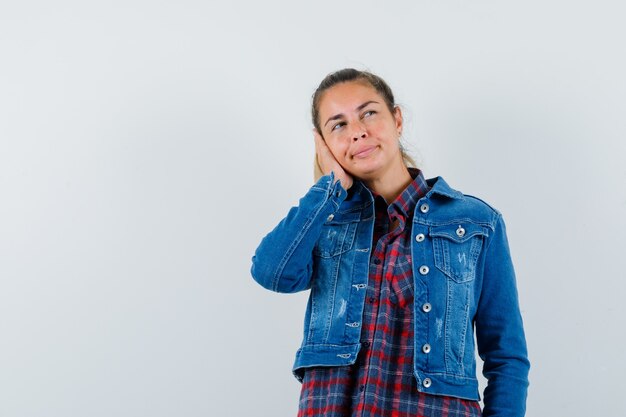 Junge Frau, die Hand auf Wange im Hemd, in der Jacke hält und hoffnungsvoll schaut. Vorderansicht.