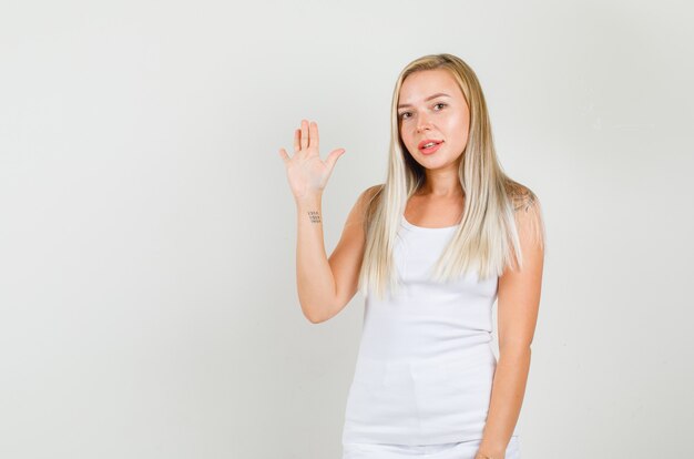 Junge Frau, die Hand winkt und im Unterhemd lächelt