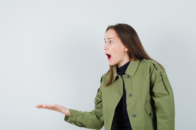 Junge Frau, die Handfläche beiseite spreizt, während sie zu jemandem in grüner Jacke, schwarzem Hemd schreit und aggressive Vorderansicht schaut.