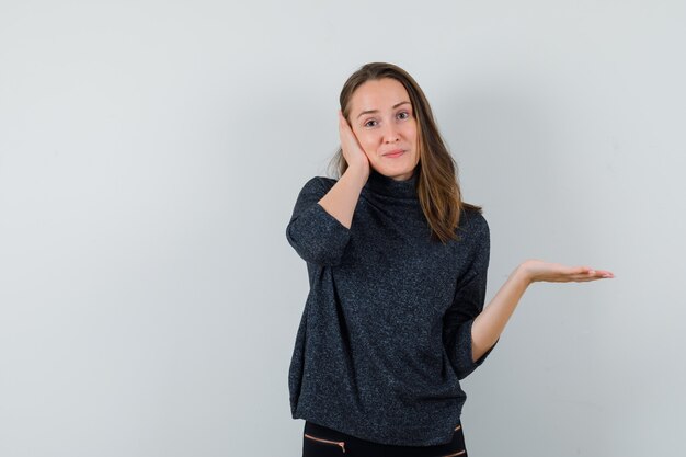 Junge Frau, die Handfläche im Hemd beiseite spreizt und verwirrt schaut