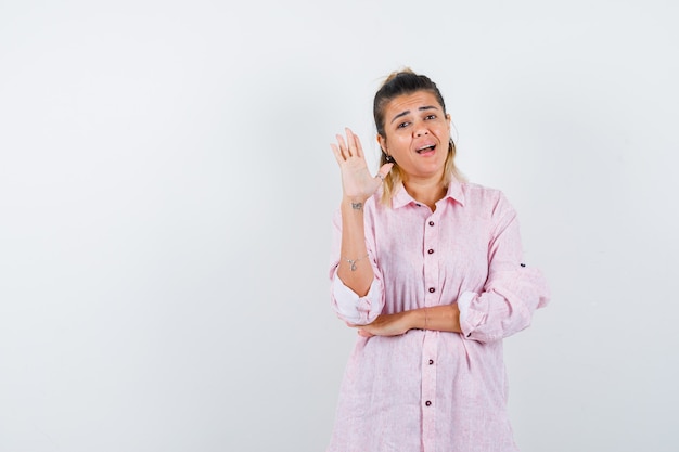 Junge Frau, die Handfläche zeigt, indem Hand in rosa Hemd erhebt und zuversichtlich schaut