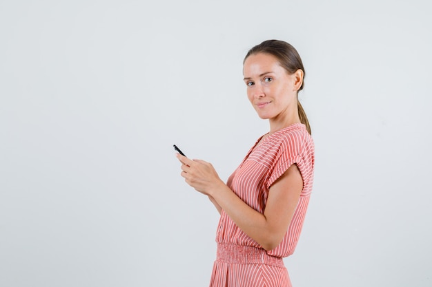 Junge Frau, die Handy im gestreiften Kleid hält und fröhlich schaut. .