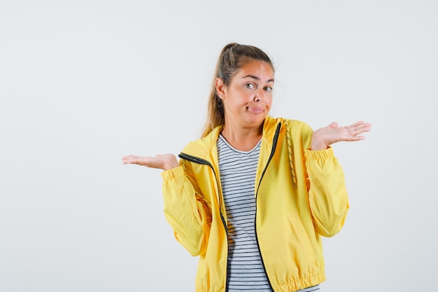 Junge Frau, die hilflose Geste in Jacke, T-Shirt zeigt und verwirrt schaut. Vorderansicht.