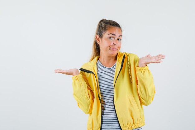 Junge Frau, die hilflose Geste in Jacke, T-Shirt zeigt und verwirrt schaut. Vorderansicht.