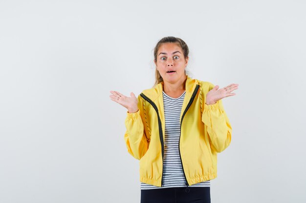 Junge Frau, die hilflose Geste in Jacke, T-Shirt zeigt und verwirrt schaut. Vorderansicht.