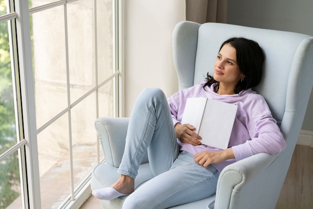 Junge Frau, die ihr Buch hält, während sie aus dem Fenster schaut