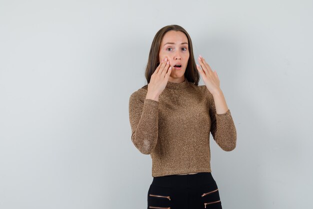 Junge Frau, die ihr Gesicht berührt, während sie vorne in goldener Bluse schaut und emotional schaut