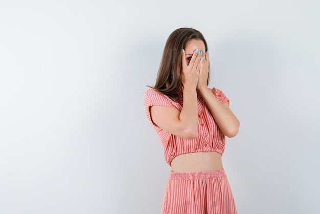 Junge Frau, die ihr Gesicht mit den Händen auf weißem Hintergrund versteckt