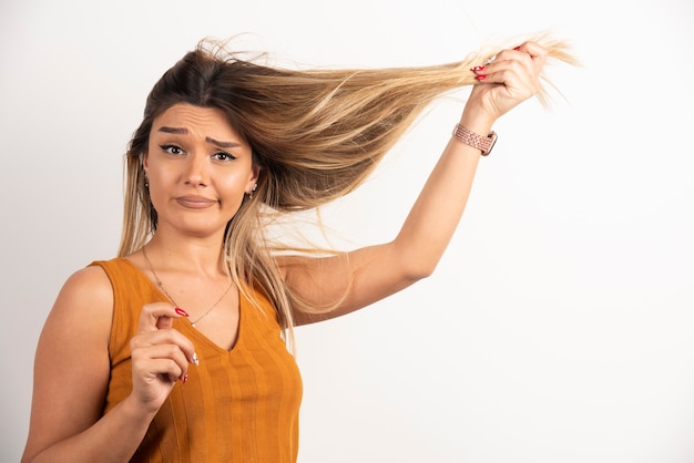 Junge Frau, die ihr Haar berührt und auf weißem Hintergrund aufwirft.