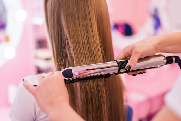 Junge Frau, die ihr Haar vom Stylisten im Salon gekräuselt bekommt. Schöner junger Friseur, der Frau im Salon neuen Haarschnitt gibt