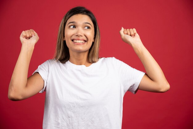 Junge Frau, die ihre Fäuste an der roten Wand erhebt.