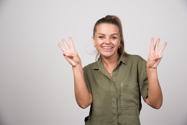 Junge Frau, die ihre Finger auf grauer Wand zeigt.