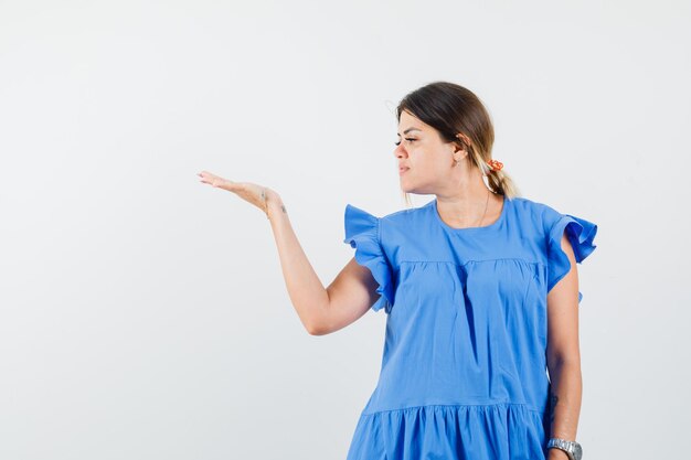 Junge Frau, die ihre Handfläche im blauen Kleid beiseite sieht