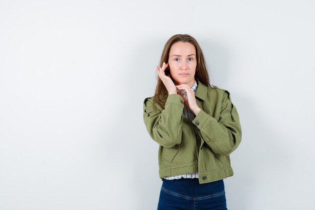 Junge Frau, die ihre Haut auf der Wange im Hemd berührt und hübsch aussieht. Vorderansicht.