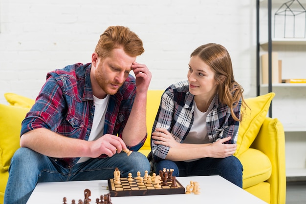Junge Frau, die ihren durchdachten Freund spielt das Schach betrachtet