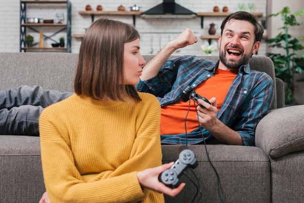 Junge Frau, die ihren Freund liegt auf dem Sofa zujubelt betrachtet, nachdem das Videospiel gewonnen worden ist